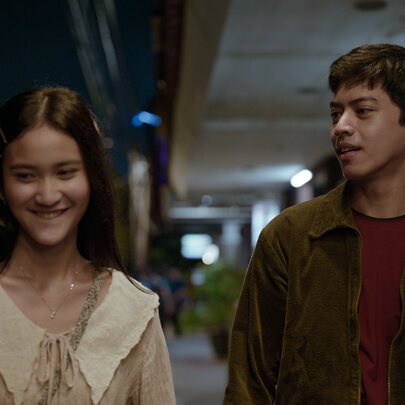 A still from the Indonesian romance film Rangga & Cinta, showing a young man and woman smiling and walking side by side. 