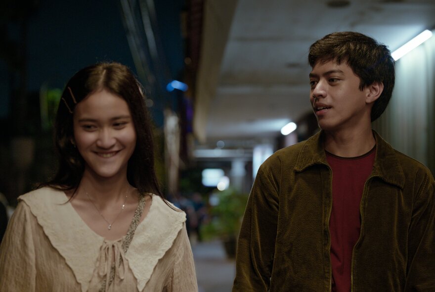 A still from the Indonesian romance film Rangga & Cinta, showing a young man and woman smiling and walking side by side. 