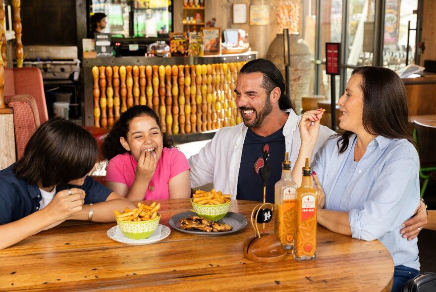 A family eating bowls of chips at a wooden table in a restaurant.