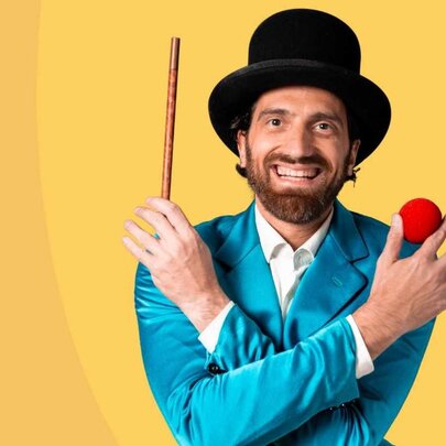 Magician wearing a top hat, holding a wand, wearing an aqua jacket and holding four red balls.