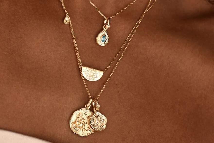 A model wearing layered gold chains with pendants including a blue stone.