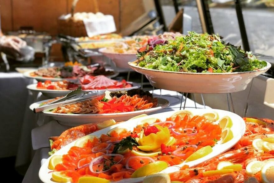 Smorgasbord of seafood, salad and meat platters beside a window.