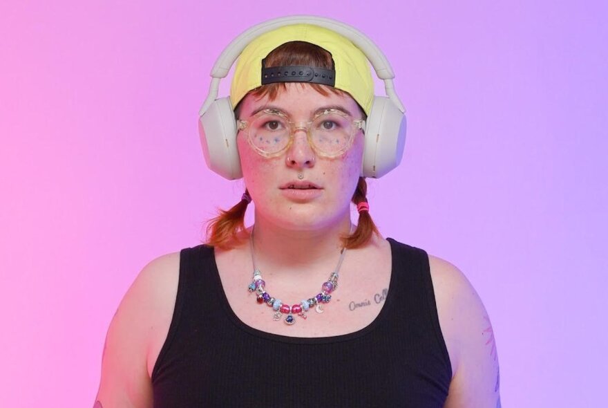 A model in a black singlet wearing a yellow cap backwards and white over the ear headphones. 