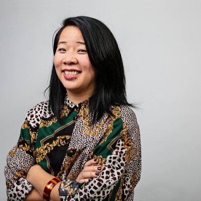 Author Beverley Wang smiling with her arms crossed wearing a pattered shirt. 