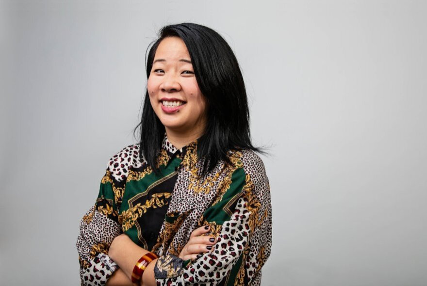 Author Beverley Wang smiling with her arms crossed wearing a pattered shirt. 