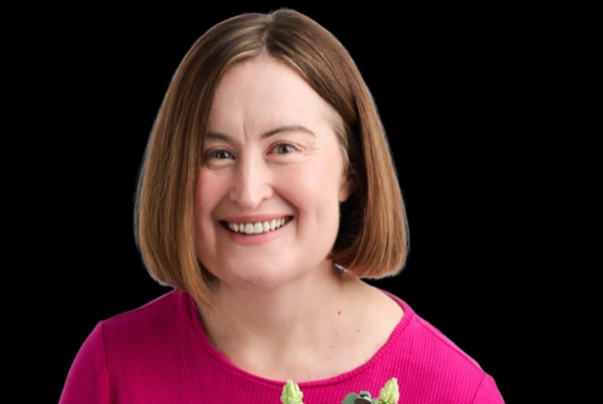 Comedian Katie Cullinan smiling against a pitch black background. 