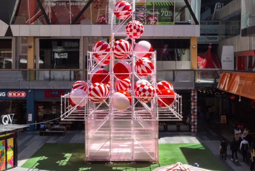 A giant Christmas tree structure made of pink scaffolding with pink and red Christmas baubles, standing on the lawn at QV Square.