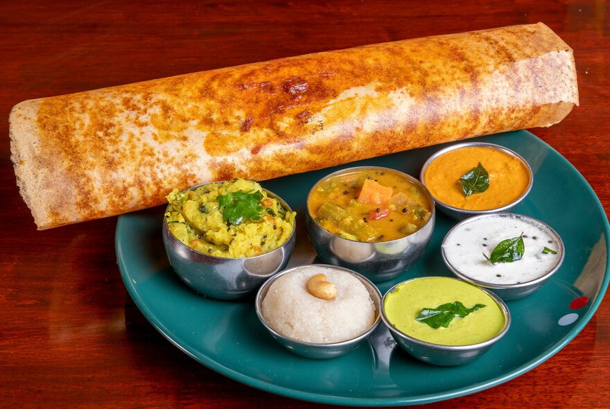 A Sri Lankan dosa with small dishes of curry, rice and sauces. 
