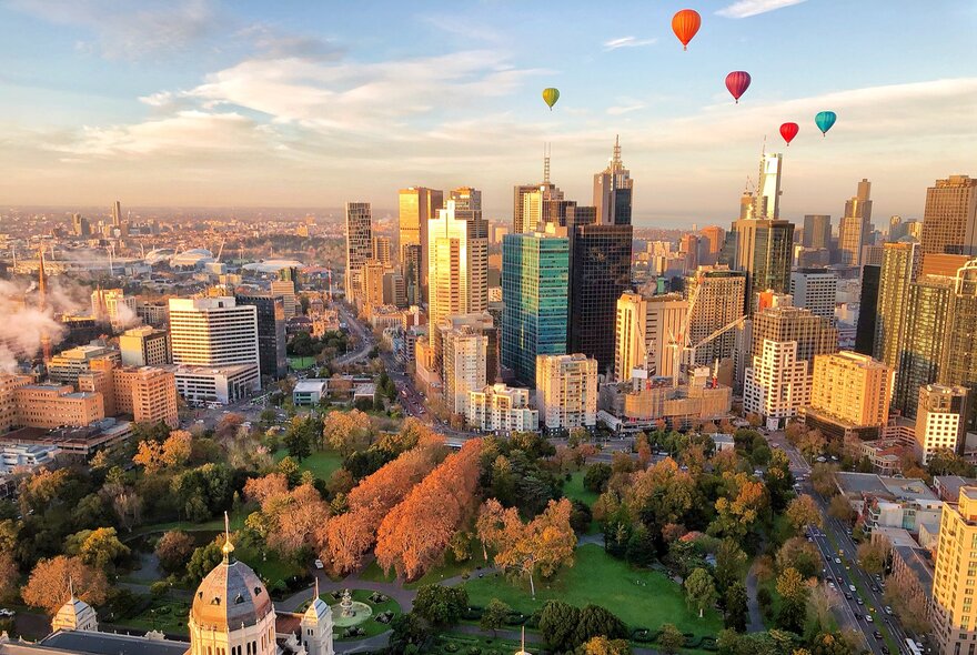 Colourful hot air balloons flying over the Melbourne city skyline and Carlton Gardens.