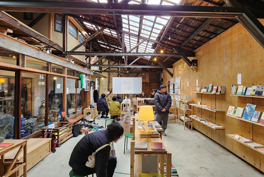 The interior of a ply-lined warehouse with artworks displayed on ply shelves and benches and people walking around.