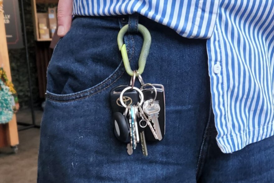 A person with a carabiner clipped to their jean belt loop, holding keys. 
