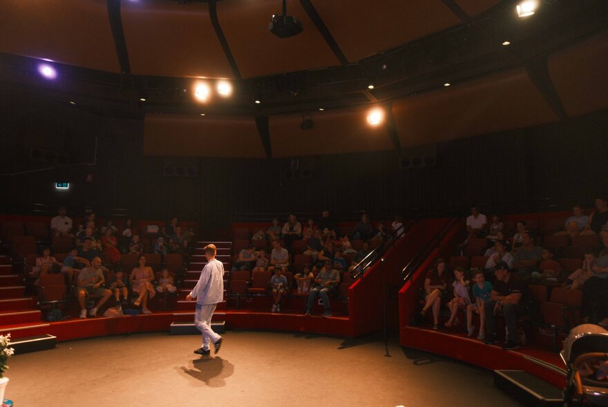 A person in white on a circular stage with an audience all around him.