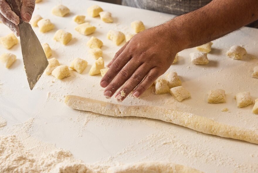 Looking down at the hands of someone cutting gnocchi shapes from long snakes of pasta dough. 