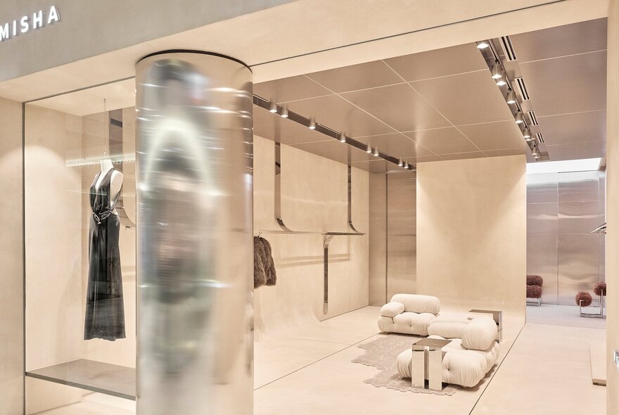 The exterior of a luxury fashion store with minimalist decor and a dress in the window. A metallic column partially blocks the view. 