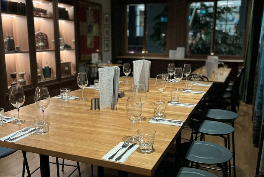 A large wooden table set with ten place settings, including water and wine glasses, napkins, cutlery and menus.