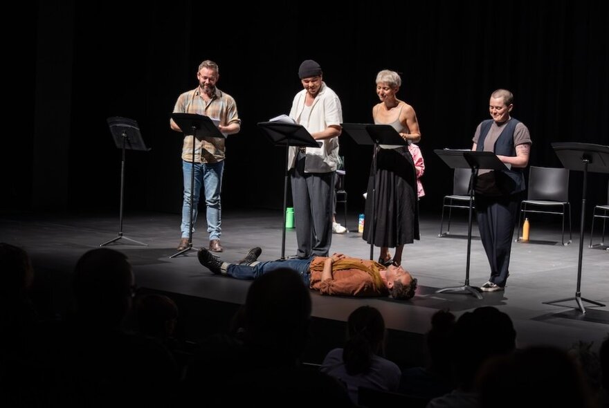 A play reading with four people standing reading on stage.