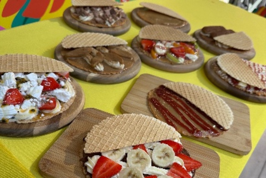 Selection of desserts arranged on wooden plates, all containing waffle biscuits, fresh fruit and icecream.