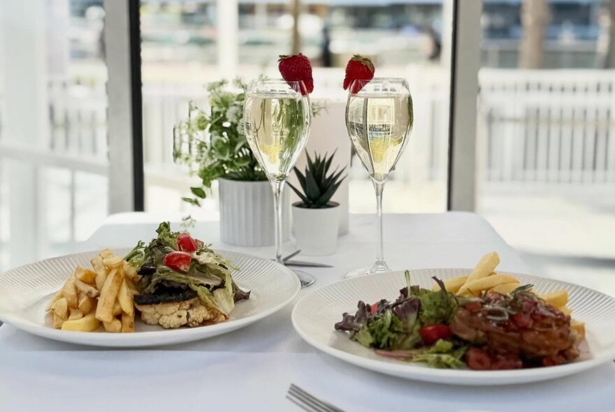 A dining table set for two with two main courses and glasses of wine, inside a gondola on the Skyline Melbourne Ferris Wheel.