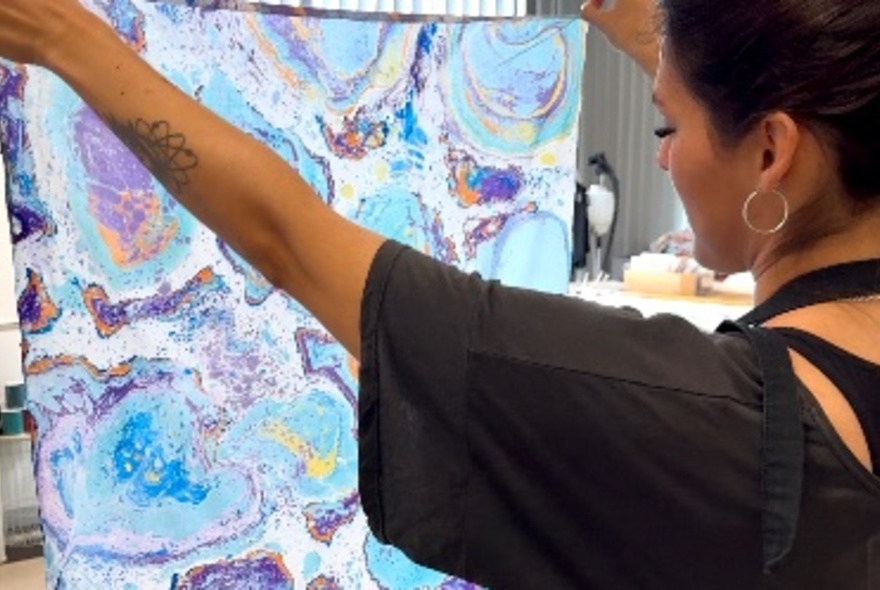 A person holding up a piece of fabric showing water marbling. 