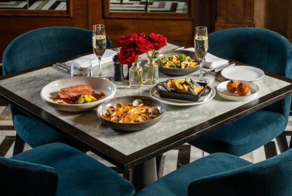 A square table set for two with a selection of share plates and two champagne glasses; four blue velvet chairs.