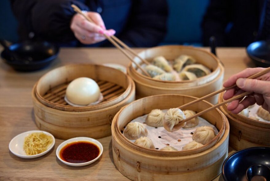 Hands holding chopsticks picking up steamed dumplings.