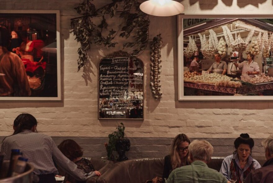 Bar interior with paintings, wall menu and organic ornaments, tables of seated patrons.
