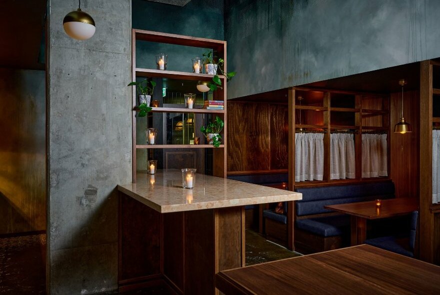 Interior of a restaurant and bar showing cosy booths, wooden tables tops, and concrete walls.