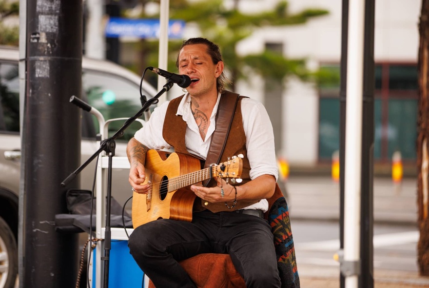 Entertainer singing and playing guitar in an outdoor setting.