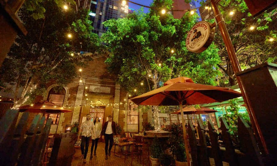 A group of three friends walking beneath fairy lights in a courtyard