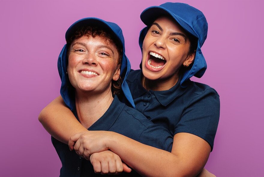Two young people wearing blue sunhats and shirts, arm in arm in front of a purple background.