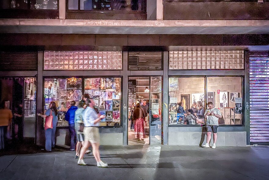 People walking past a venue with an open door and pinkish lighting. 