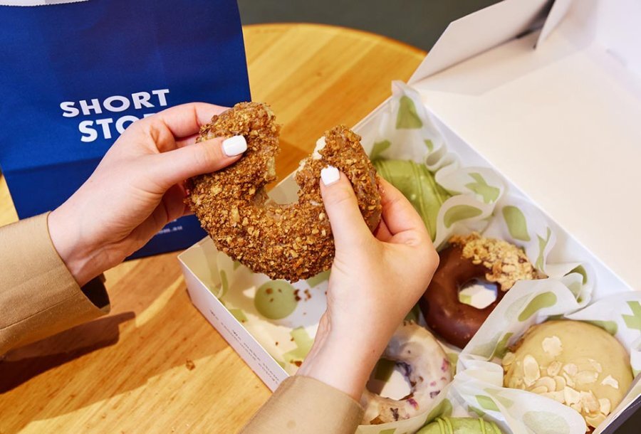 Nutty doughnut being torn in half above a box of more doughnuts.