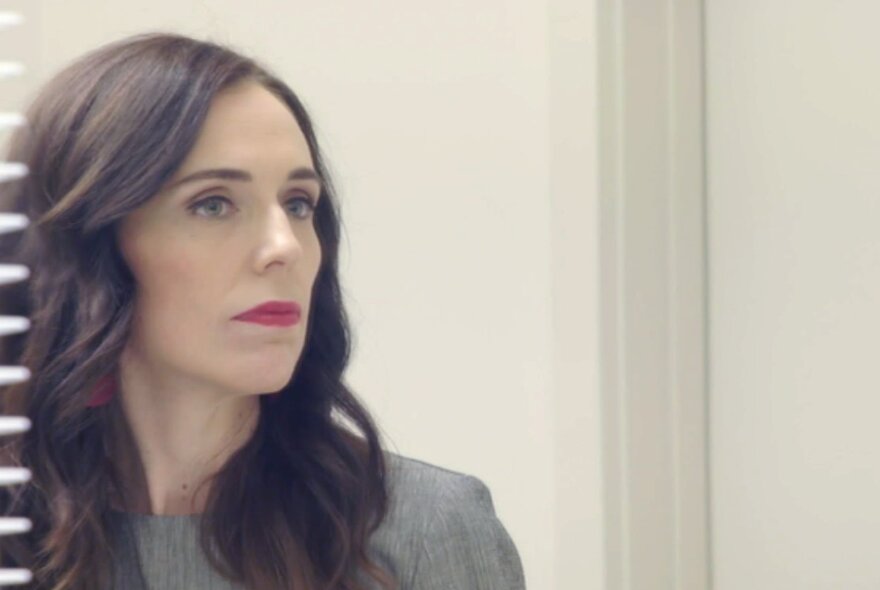 A still from a documentary about Jacinda Ardern showing her looking into a mirror with a serious expression. 
