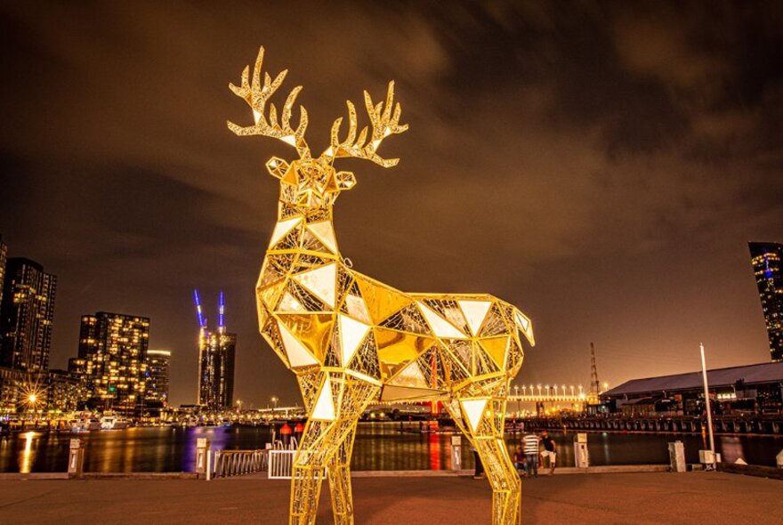 Large golden reindeer statue in front of Melbourne city skyline.