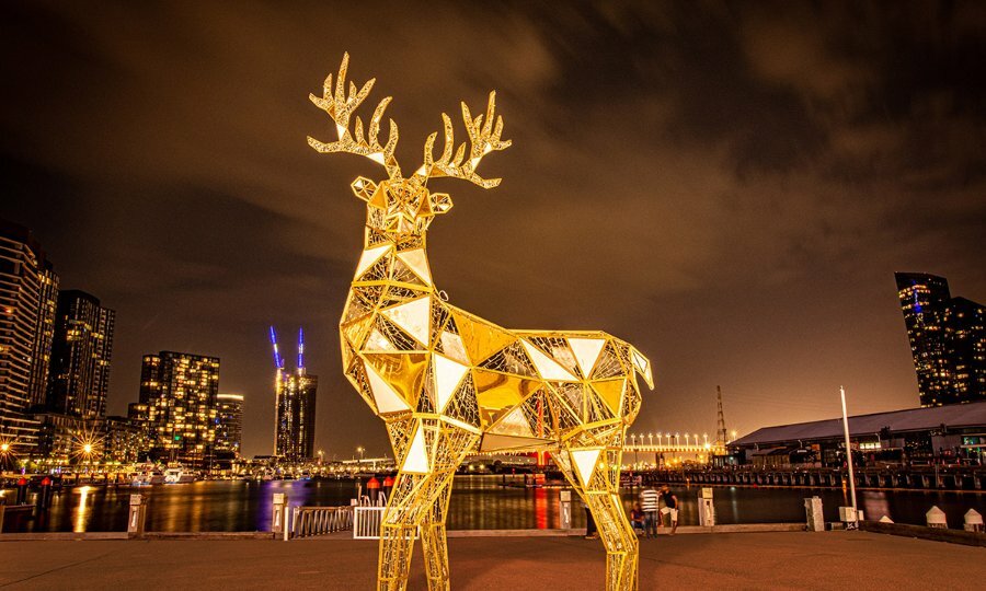 Large golden reindeer statue in front of Melbourne city skyline.