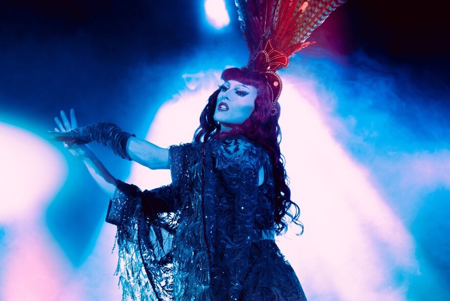 A burlesque dancer with a tall headdress performing with spotlights behind her. 