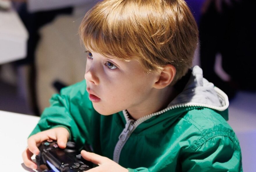 A young child holding a video game controller  with their hands and looking at a screen that is outside of the frame.