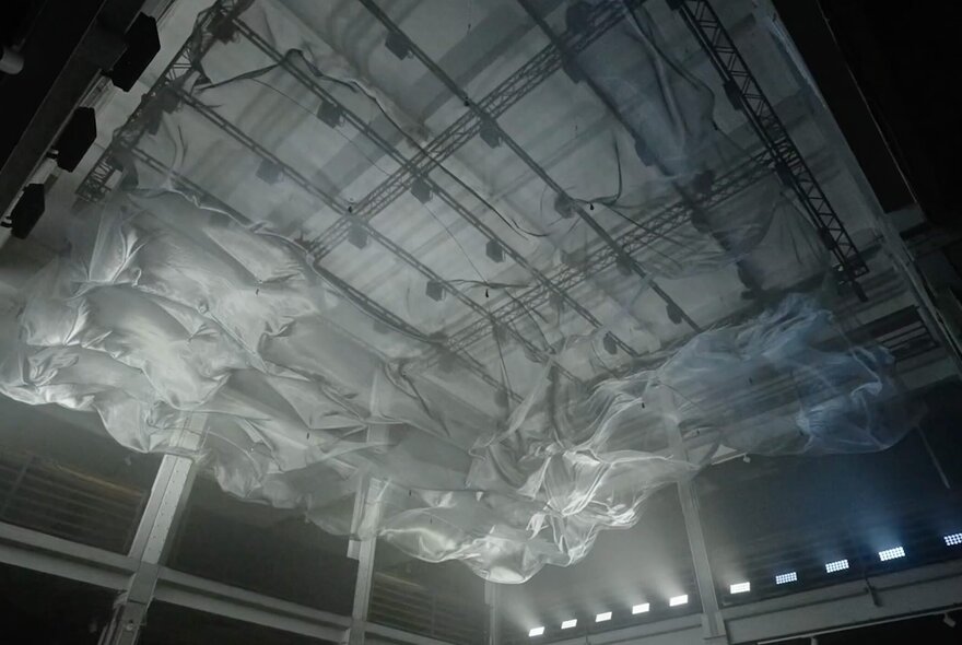 Sculptural art installation of billowing fabric against a ceiling, spot-lit from underneath.