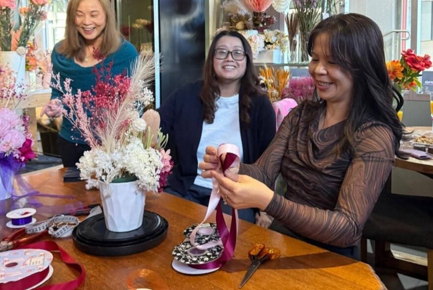 A woman demonstrating flower arranging to several women looking on and smiling. 