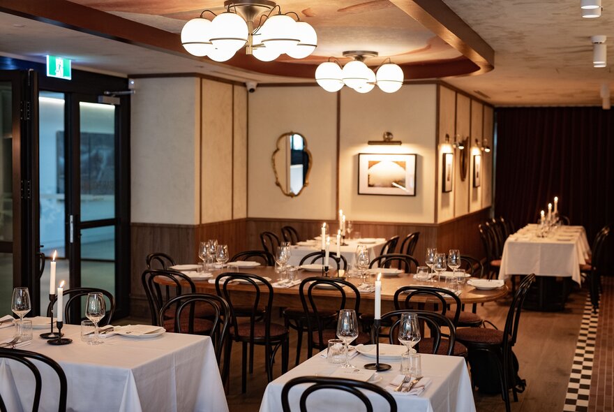 Restaurant interior with a mix of small and large tables, overhead lighting.