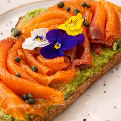 Smoked salmon on a slice of bread on a plate, garnished with colourful pansies and capers.