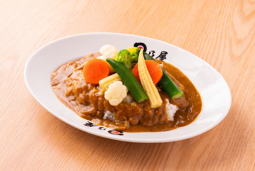 Japanese curry with vegetables on top in a white bowl on a wooden surface.