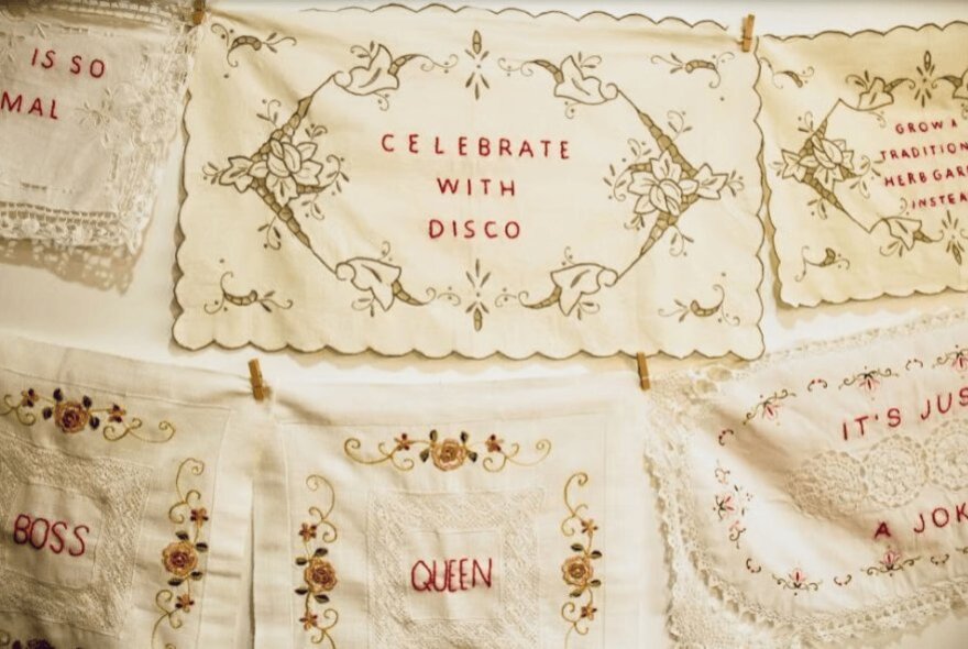 Vintage linens with red embroidery by artist Sonia Zymantas, incorporating contemporary text into traditional craft.