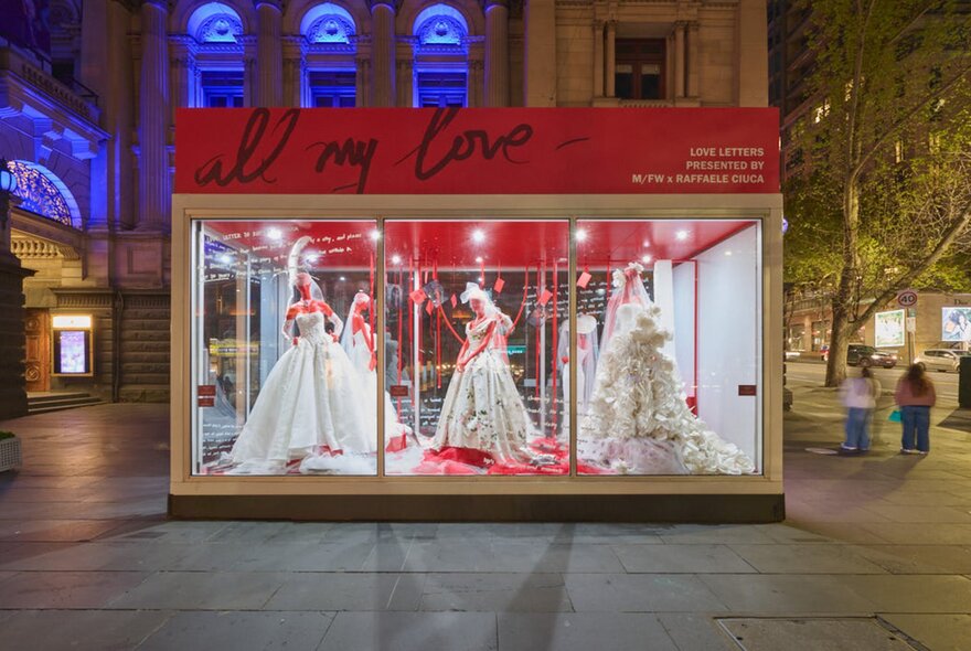 A transparent cube with ball gowns on mannequins displayed inside