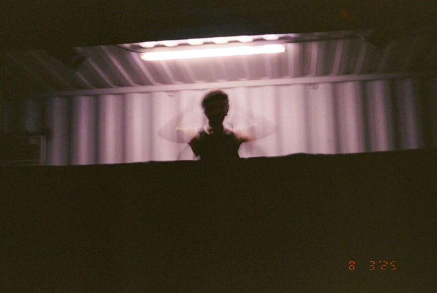 A DJ in a dimly lit DJ booth with blurred arms as if moving quickly.