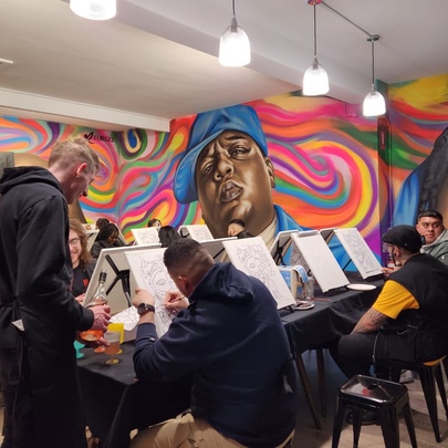 Several rows of people painting on canvases in a room with large, wall murals.