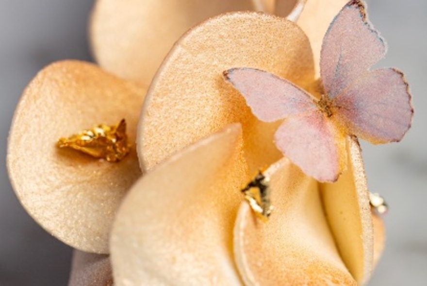 A tiny butterfly made from sugar, resting on a yellow coloured floral cake decoration.