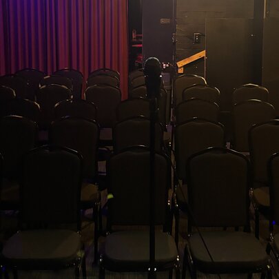 A dark image showing an empty theatre with rows of empty seats in front of a microphone on a stand.