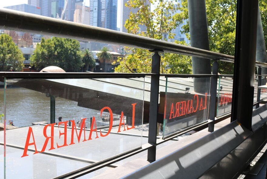 A view of the Yarra River and some Melbourne buildings through the glass balcony fence of La Camera restaurant.