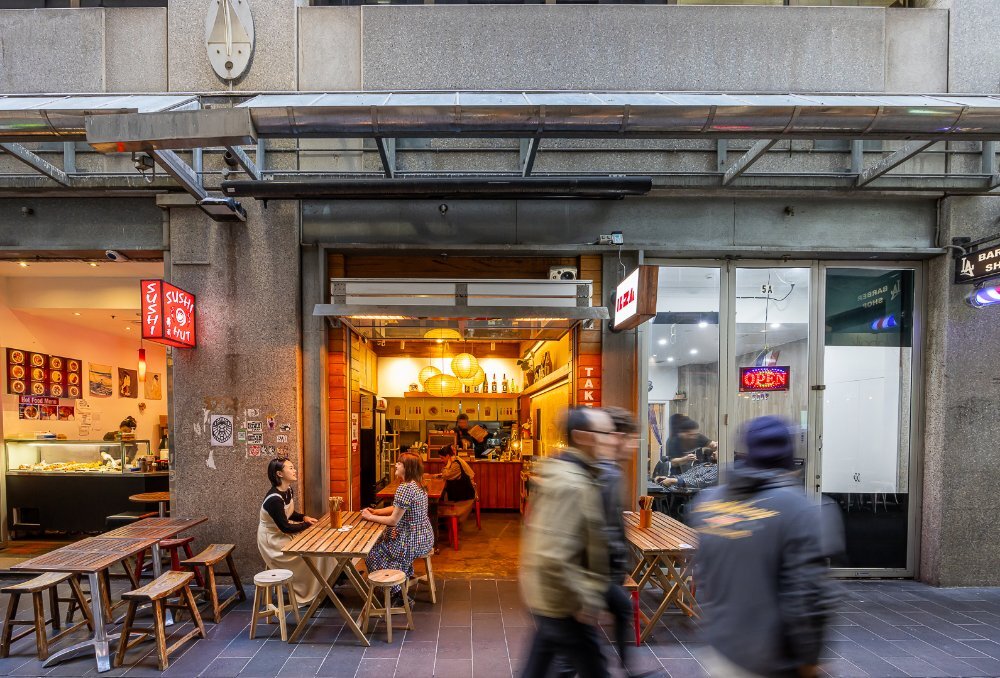 People dining outside a glowing laneway cafe. 